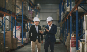 management having discussion at warehouse with white hardhat using digital tablet
